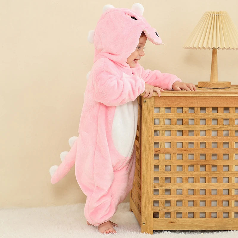 Den här bilden visar en gullig och mjuk rosa T-Rex maskeraddräkt för barn, tillverkad i bekvämt flanellmaterial med ett detaljerat fjällmönster. Dräkten har en fastsatt huva med vita tänder och ögon samt en stoppad svans baktill, vilket gör den perfekt för både maskerad och rolig lek.
