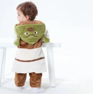 Den här bilden visar en gullig Shrek-maskeraddräkt för barn, bestående av en mjuk, ljusbrun överdel med väst och matchande gröna byxor. Dräkten fullbordas av en karakteristisk grön huva med Shreks ikoniska öron, vilket skapar ett roligt och igenkännbart utseende för maskerad eller lek.