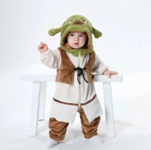 Den här bilden visar en rolig Shrek-maskeraddräkt för barn, bestående av en beige överdel med påsydd väst, rutiga byxor och en grön mask med de karakteristiska trollöron. Dräkten är designad i mjuka material, som gör den bekväm för småbarn att ha på sig för maskerad eller lek.