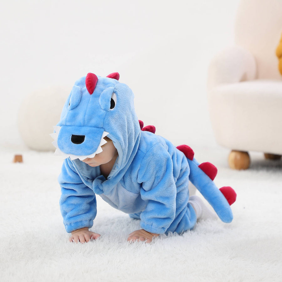 Bilden visar en gullig och mjuk blå T-Rex maskeraddräkt för barn, sett från sidan för att framhäva den långa svansen med mörkblå taggar. Dräkten är gjord av bekvämt flanellmaterial med en vit mage och en detaljerad huva, som föreställer ett dinosauriehuvud med ögon och små tänder.